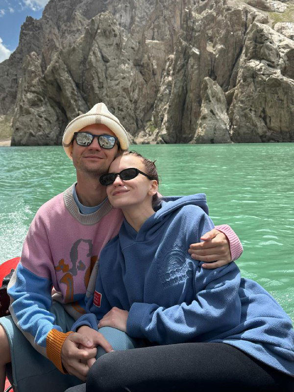 Пара на лодке в бирюзовом горном озере: улыбки, солнцезащитные очки и спокойная водная гладь на фоне скалистых берегов.