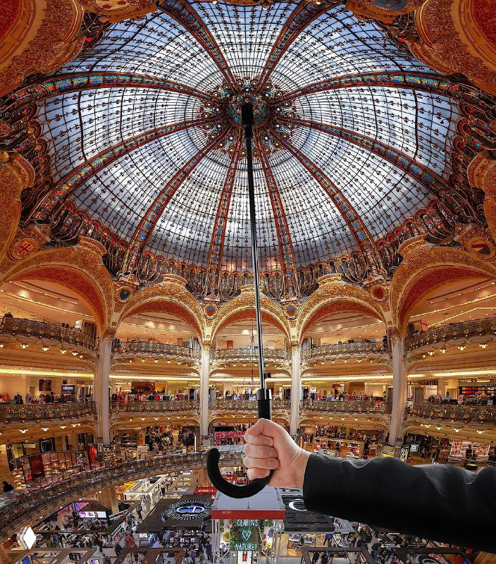 Интерьер роскошного торгового пассажа с куполом и витражами; на переднем плане рука держит ручку зонта — контраст между деталями и пространством.