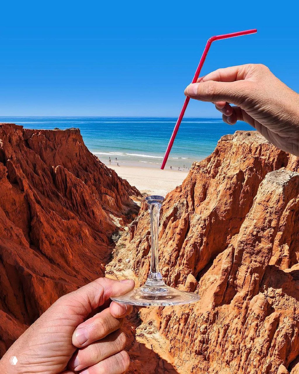 Руки держат бокал и соломинку на фоне красных утёсов и пляжа; композиция создаёт оптическую игру с масштабом и создает визуальную метафору.