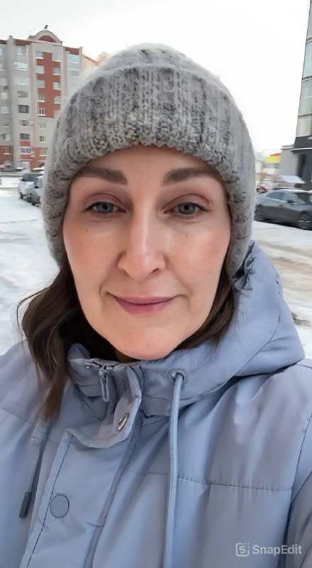 Тот же кадр селфи с заметным в правом нижнем углу логотипом SnapEdit; зимняя шапка, куртка и размытый городской фон позади.