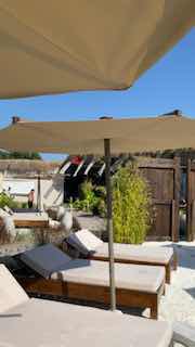 Солнечные шезлонги и зонты у бассейна на открытой террасе в летний день, показывающие атмосферу пляжного отдыха и релаксации.