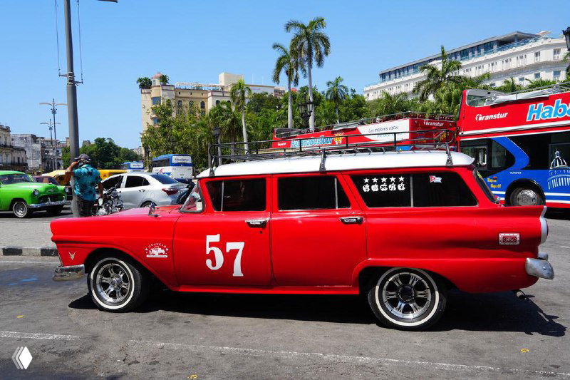 Ярко-красный ретро-универсал с номером 57 стоит на улице Гаваны на фоне тропических пальм и городских зданий.