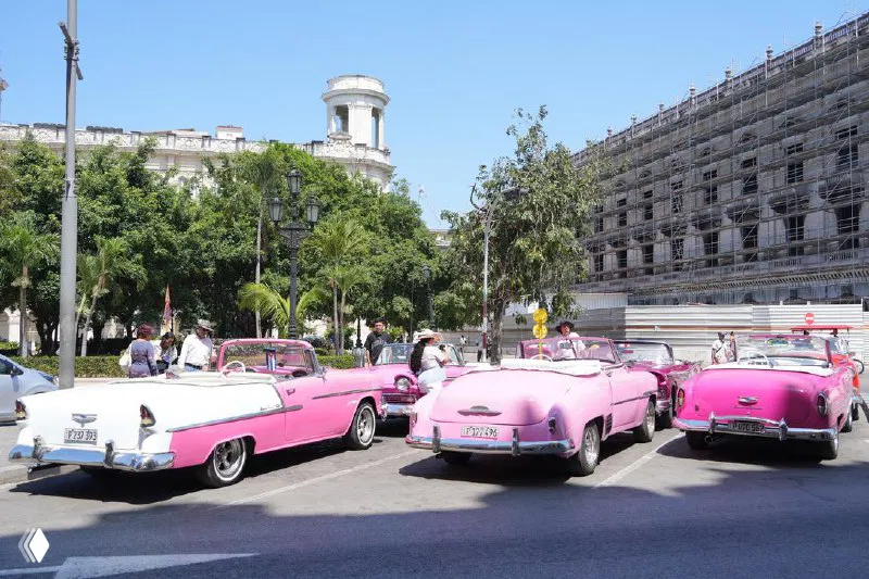 Несколько розовых классических кабриолетов припаркованы у городской площади Гаваны — туристический кадр с ретро-авто и туристами.