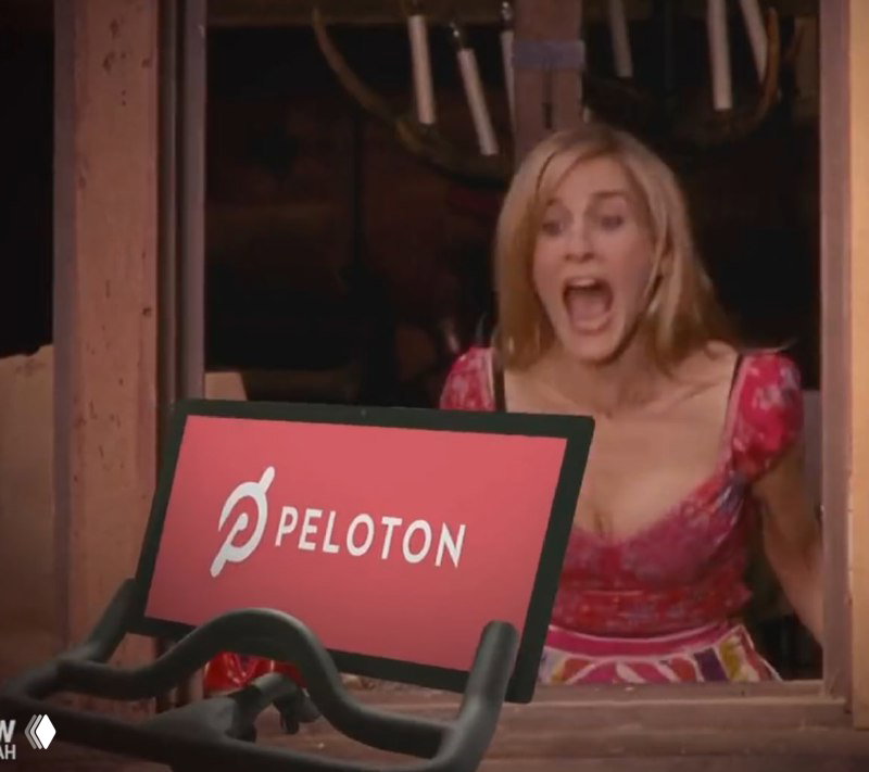 Кадр из сериала: женщина эмоционально кричит за велотренажёром с логотипом Peloton — сцена, связанная с сюжетом и падением акций PTON.