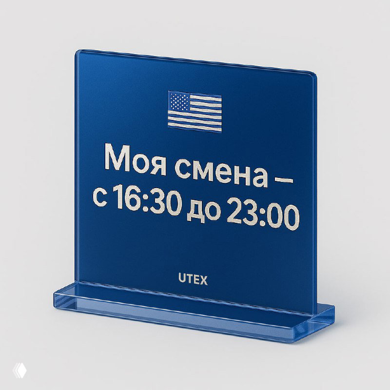 Синяя акриловая табличка UTEX с белой надписью «Моя смена — с 16:30 до 23:00» и мини-флагом США, фото демонстрирует настольный аксессуар в корпоративном стиле.