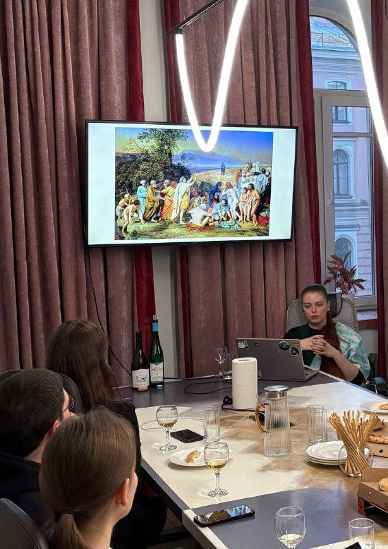 Зал с участниками, столами и бокалами; на экране воспроизведена картина — сочетание лекции, визуального ряда и дегустации в рамках творческого вечера.