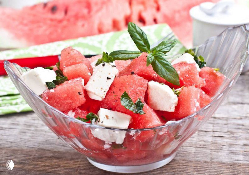 Арбузный салат с кубиками феты, листьями базилика и мятой в прозрачной миске — яркая летняя подача, сочность и свежесть ингредиентов.