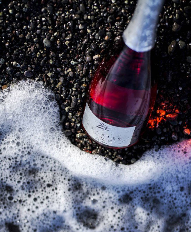 Бутылка розового вина на каменистом берегу с пеной воды вокруг — атмосферный снимок, подчеркивающий стильное представление вина.