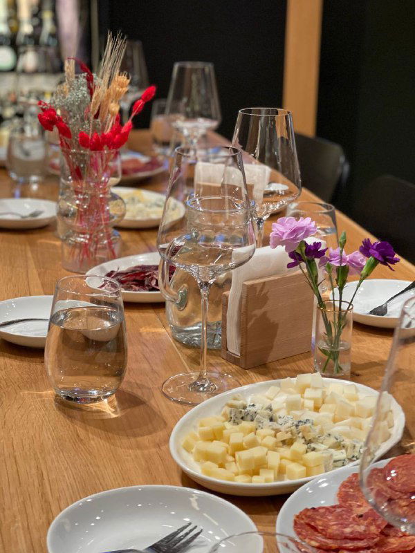 Убранный стол для дегустации: бокалы, тарелки с сыром и закусками, небольшие цветочные композиции и сервировка для пятничного вечера.