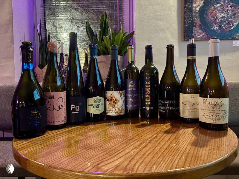 Ряд открытых бутылок крымских вин на деревянном столе — представленные образцы дегустации с различными этикетками и стилями.