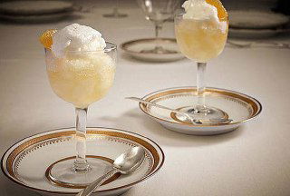 Две изящные порции пунша в бокалах с лимонным сорбе и украшением; сервировка десертного коктейля Punch à la Romaine в элегантной обстановке.
