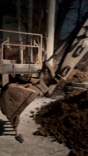 Ночной кадр: экскаватор роет котлован, видны земляные работы и строительная техника на тёмном фоне, рабочая площадка.