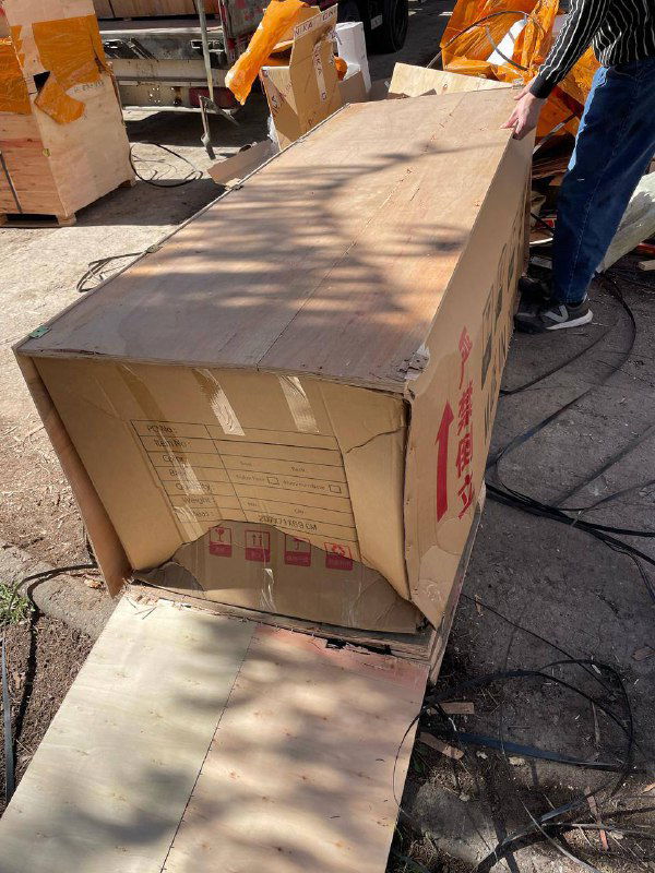 Большая картонная коробка с распахнутой крышкой и раздавленным углом: товар внутри частично выставлен наружу, нарушена целостность упаковки.