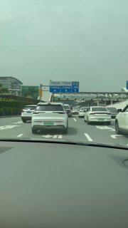 Вид из автомобиля на многополосную загруженную трассу в пригороде Гуанчжоу (Фошань): множество машин, заторы, заметны зелёные номера электромобилей.