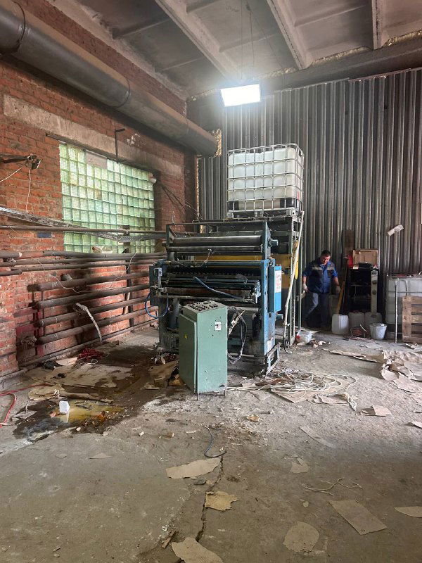 Внутренний вид заброшенного производственного цеха: старые станки, грязный пол, разбросанные материалы и стеклоблоки в стенах.