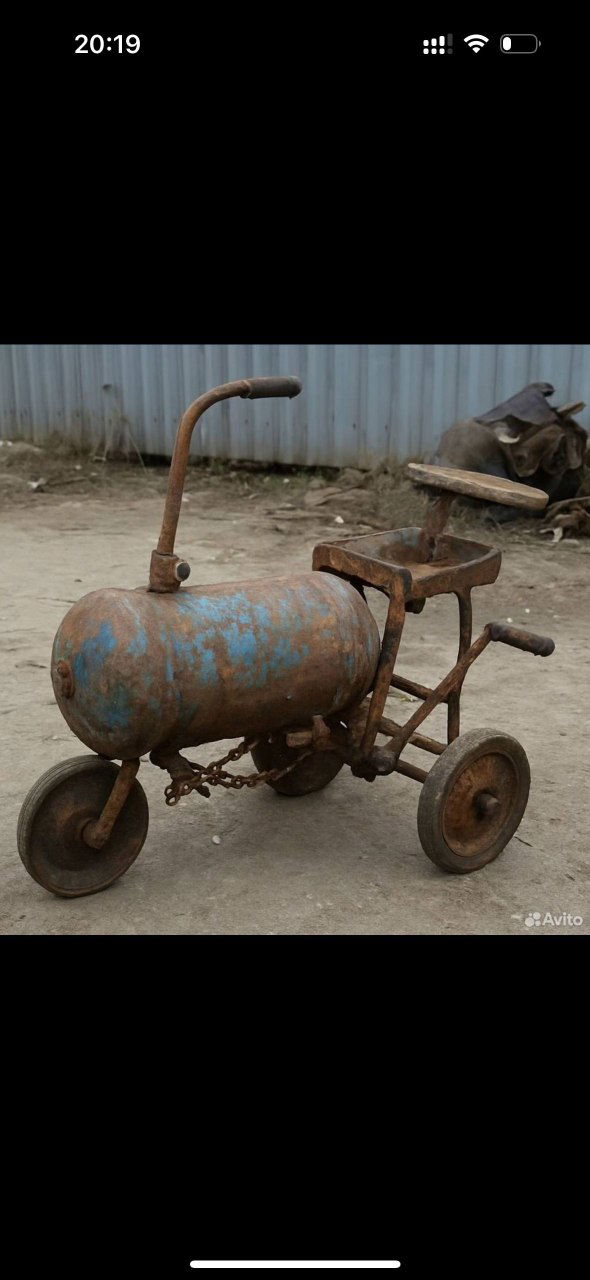 Фото из объявления на Авито: трёхколёсный самодельный агрегат из металлического баллона и рам, следы ржавчины, цепи и сломанные детали на фоне заборов.