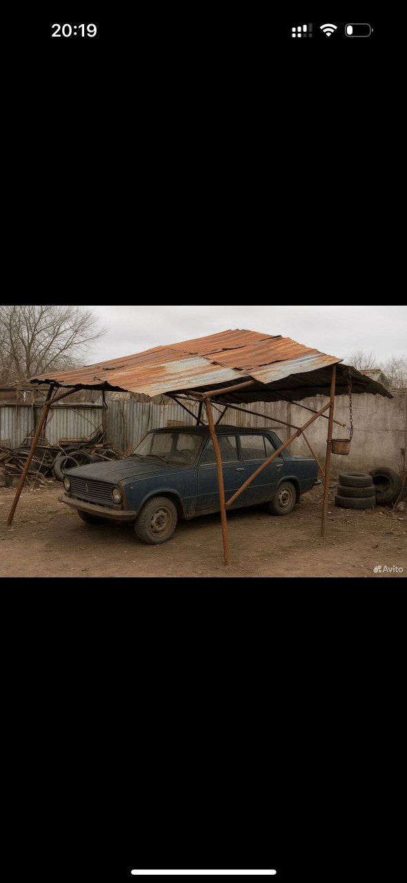 Фото из объявления на Авито: старая машина под самодельным навесом из ржавого профиля, вокруг — автозапчасти и свалка металла у мастерской.