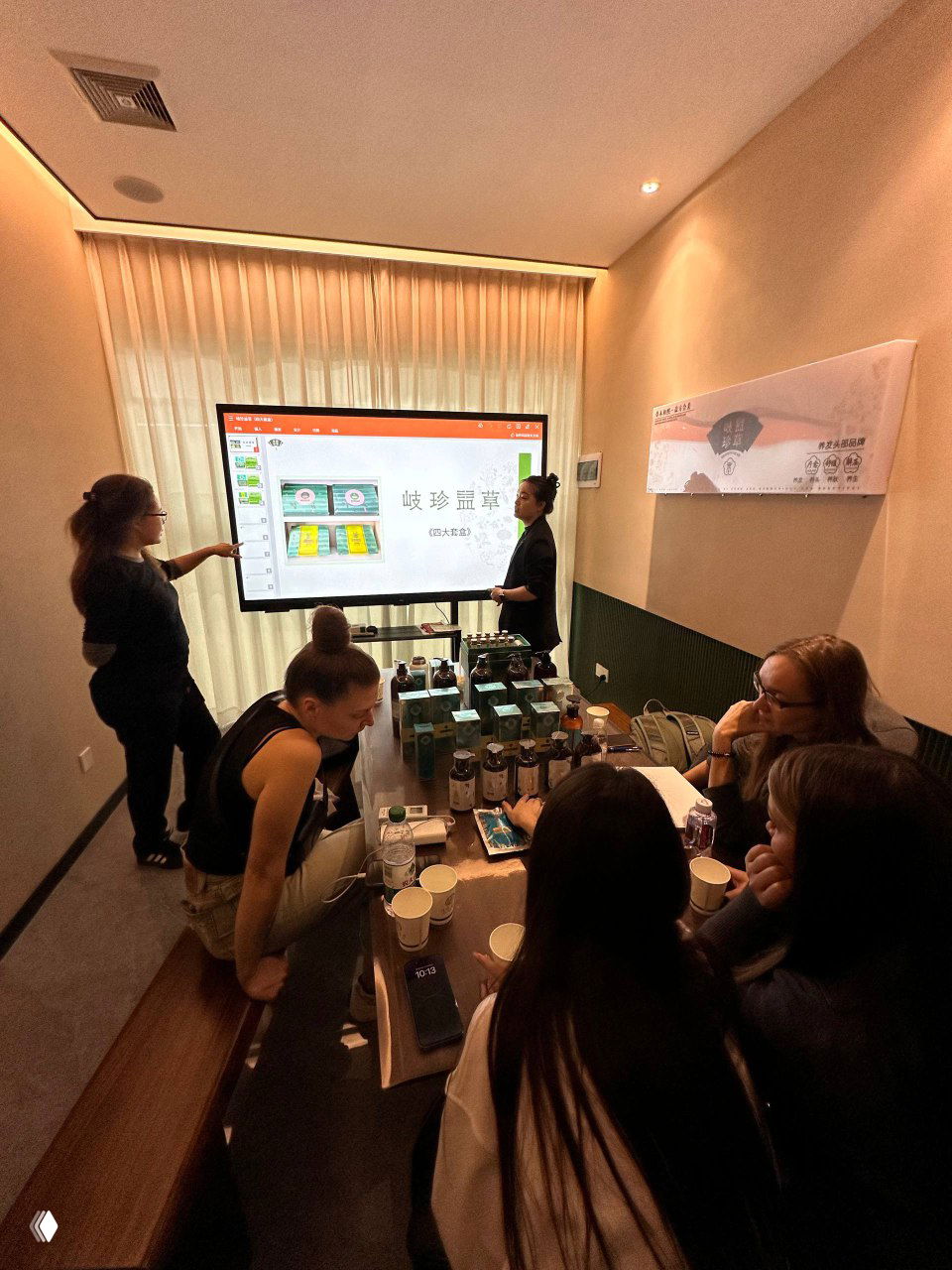 Комната переговоров на презентации: люди сидят вокруг стола, на нём образцы продукции и демонстрационные материалы, идёт презентация.