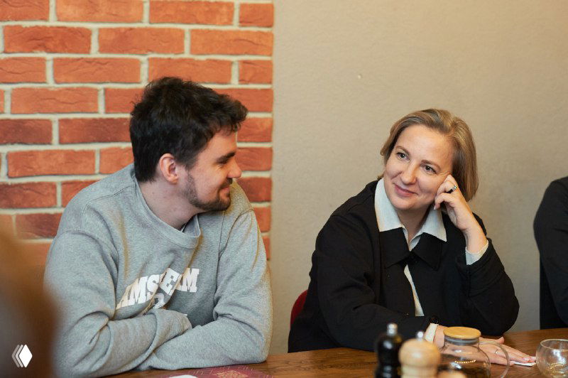 Участница тренинга улыбается в ответ на реплику коллеги: кадр показывает доверительную атмосферу и вовлечённость в групповую работу.