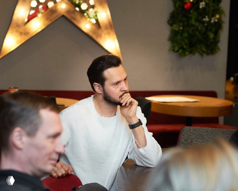 Крупный план задумчивого участника в белом свитере, внимательно слушающего разбор, выражение сосредоточенности и внутренней работы над запросом.