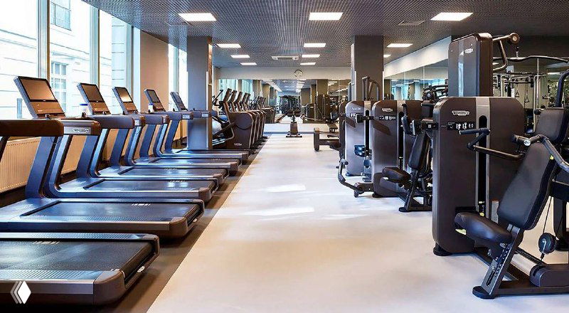 Тренажёры и беговые дорожки в просторном зале спортивного клуба, аккуратно расставленное современное оборудование.
