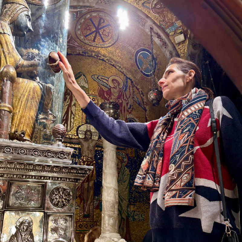 Момент в алтарном зале: автор прикладывает руку к статуе или реликвии рядом с мозаикой, свечи и золотые орнаменты создают интимную атмосферу.