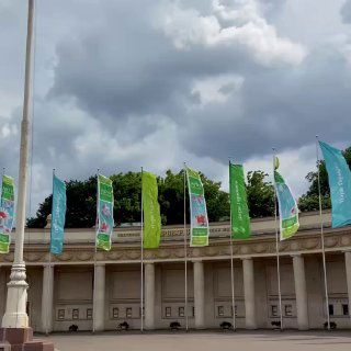 Флаги и колоннада в Парке Горького под тёмными грозовыми тучами, вид на фасад парковой постройки и развевающиеся баннеры фестиваля.