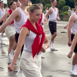 Парад физкультурников в Парке Горького: группа молодых людей в белой форме марширует по аллее при пасмурной погоде.