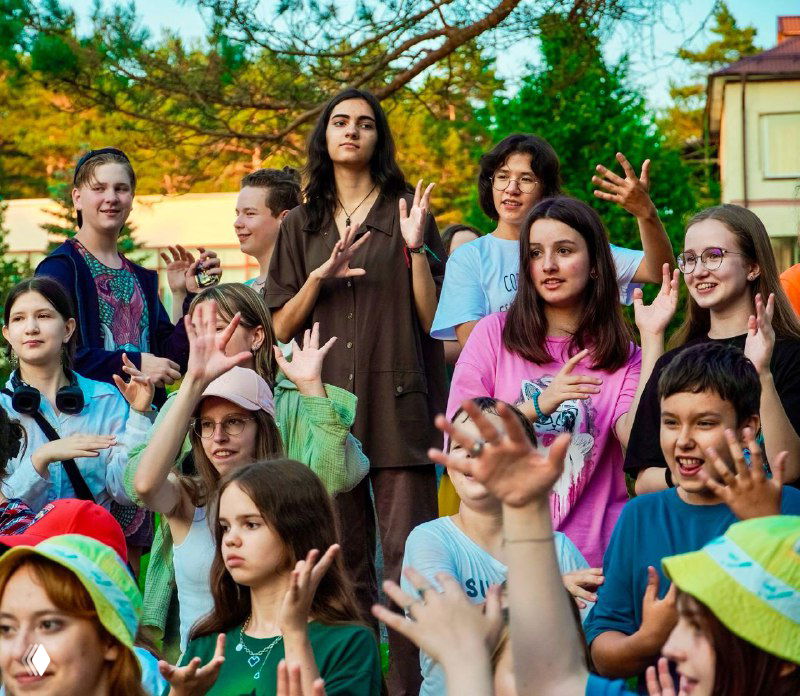Большая разношёрстная группа детей и подростков на летнем загородном лагере на открытом воздухе: яркая одежда, живые эмоции, командные активности и отдыхающая атмосфера.