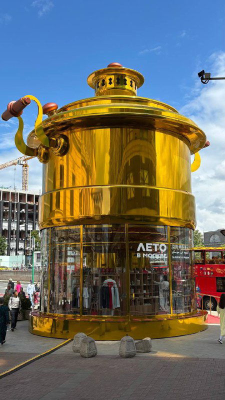 Крупный золотой арт-павильон в форме самовара на городской площади Москвы с логотипом проекта «Лето в Москве» и людьми у входа.