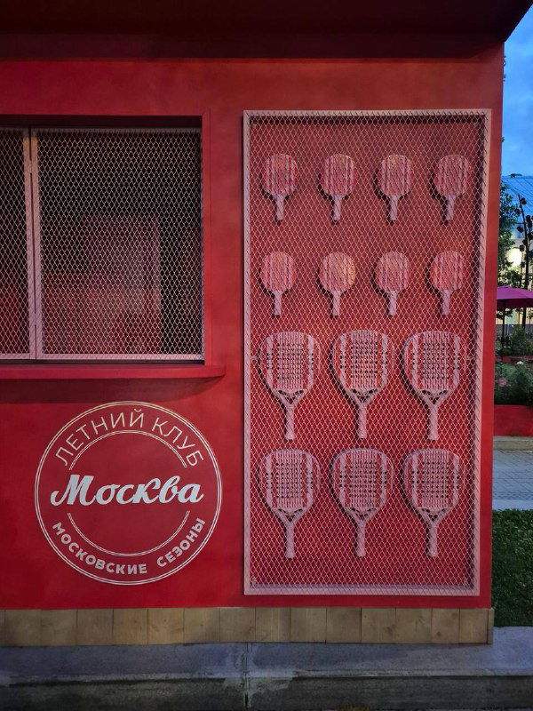 Красная декоративная стенка с графикой теннисных ракет и логотипом 'Москва' — элемент визуального оформления одного из торговых павильонов.