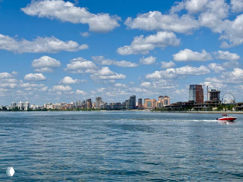Широкий вид реки Казанки с зеркальной водой, городской панорамой на горизонте и моторной лодкой, разрезающей спокойную поверхность реки.