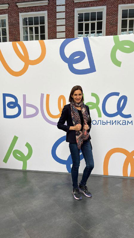 Полноформатный снимок автора на фоне брендированной фотозоны фестиваля школьников ВШЭ с яркими буквами и логотипами университета, посетители и оформление мероприятия.