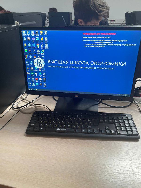 Рабочее место в компьютерном классе ВШЭ: монитор с экраном загрузки университета, клавиатура и мышь на столе — вид изнутри кампуса и учебной инфраструктуры.