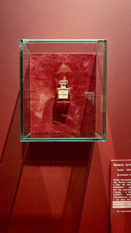 Стеклянная витрина с маленьким флаконом духов на бархатном красном фоне — музейный экспонат, символ женственности эпохи 20–30-х годов.