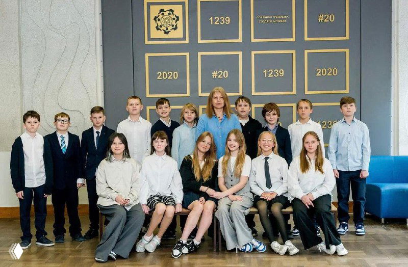 Групповой классный снимок школьников и учителя в фойе или актовом зале — официальная фотография с доской наград и информацией о школе на фоне.