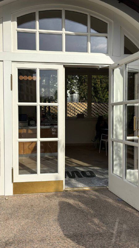 Открытая дверная арка с большими стеклянными створками: вход в кафе с белыми рамами и приглашающей атмосферой минималистичного интерьера.