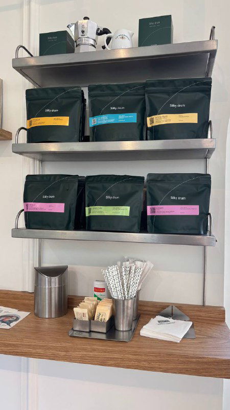 Полки с упаковками кофе и аксессуарами: ассортимент зернового кофе в фирменной упаковке и стильный минималистичный стеллаж в интерьере.