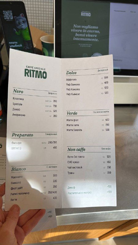 Кофейное меню на листке бумаги в руках — цены и ассортимент напитков Ritmo, вид с близкого расстояния на список кофе и позиции меню заведения.
