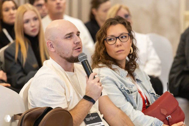 Андрей и Виктория в зале с аудиторией: мужчина держит микрофон, женщина рядом, участники слушают выступление.