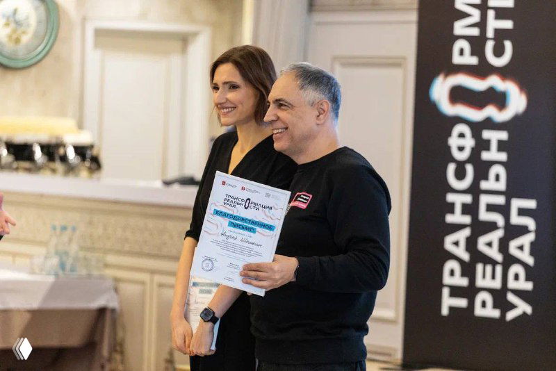 Виктория и мужчина получают сертификат или благодарность на сцене форума, улыбки и деловая атмосфера мероприятия.