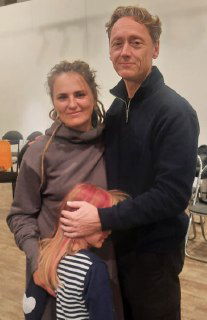 Женщина стоит рядом со взрослым мужчиной, рядом ребёнок обнимается за ногу — сцена после тренинга или встречи, эмоциональная поддержка и близость между людьми.