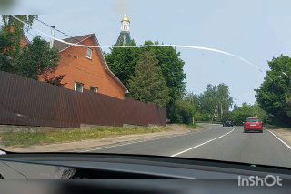 Дорога мимо деревенского пейзажа с куполом храма на заднем плане; кадр даёт контекст расположения ретрита в пригородной местности