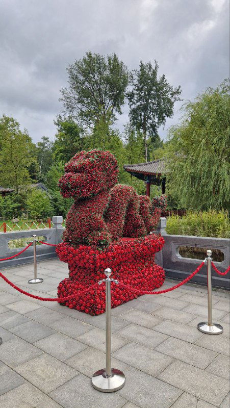 Декоративная скульптура, сложенная из цветов в форме фигуры на площадке у входа в композицию парка «Хуамин», окружена ограждением.