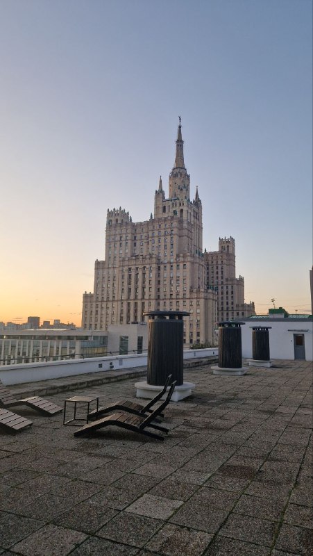 Крыша Дома Наркомфина с видом на одну из московских высоток: плоская кровля, городской пейзаж и вечернее небо.