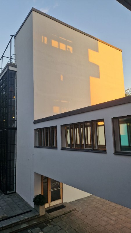 Перспективный вид на белые фасады и переходы Дома Наркомфина: простые геометрические формы и тёплое вечернее освещение.