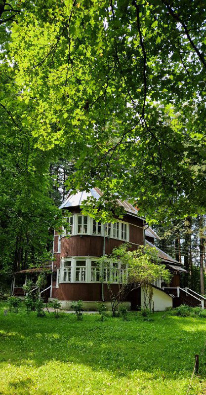 Фасад дома-музея Пастернака среди зелёных деревьев: двухэтажный деревянный дом окружённый садом и естественной растительностью Переделкина.