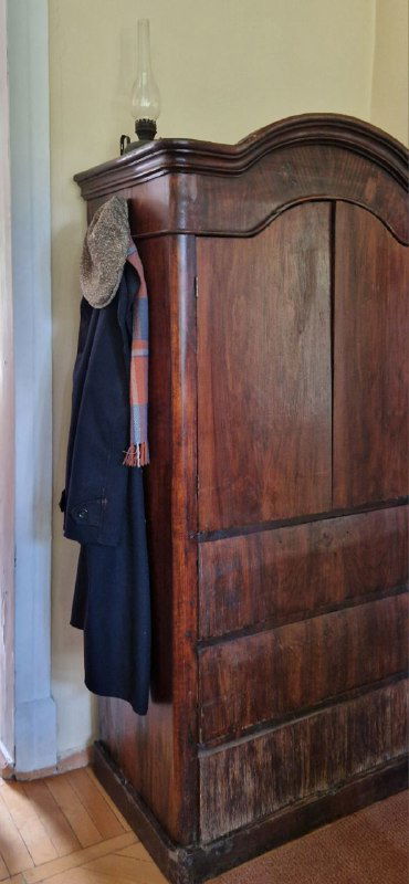 Деревянный шкаф в музее с висящим пальто и кепкой — экспонат, создающий эффект присутствия хозяина в доме-музее.