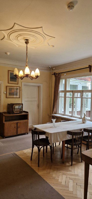 Столовая или гостиная в доме-музее: длинный стол, подвесная люстра и оконные проёмы, создающие атмосферу дачного дома начала XX века.