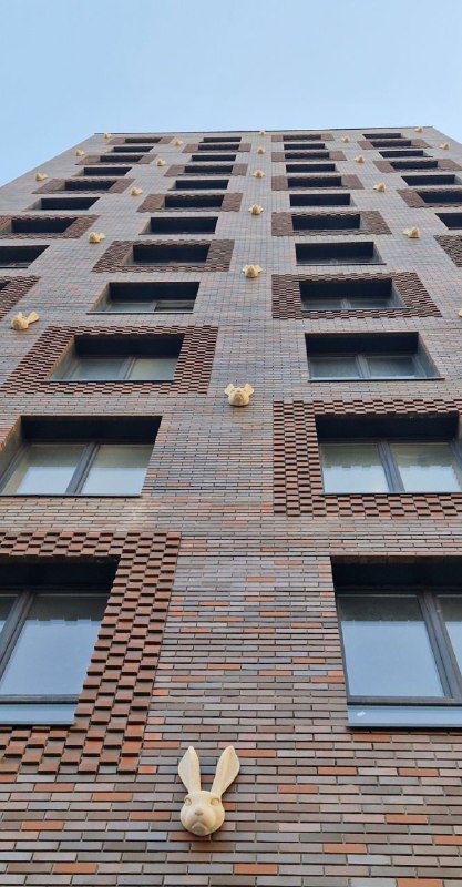 Фрагмент кирпичного фасада «Дома с зайцами» с одной из крупных масок зайца, вид снизу вверх, декоративные элементы и окна здания.